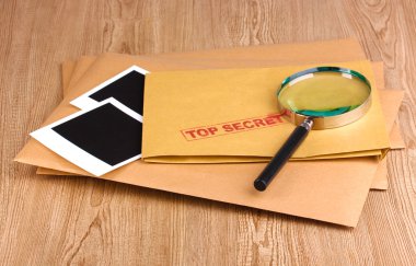 Envelopes with top secret stamp with photo papers and magnifying glass on wooden background clipart