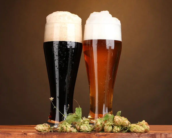 Cerveza negra y dorada en vasos y lúpulo sobre mesa de madera sobre fondo marrón —  Fotos de Stock