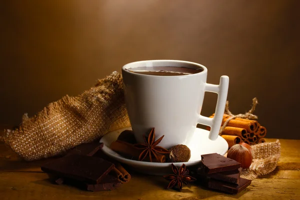 Cup of hot chocolate, cinnamon sticks, nuts and chocolate on wooden table on brown background — Stock Photo, Image