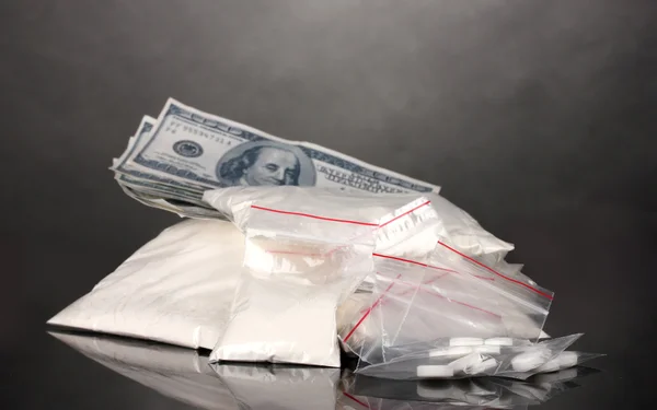 Kokain a drogy v balíčcích, dolary na šedém pozadí — Stock fotografie