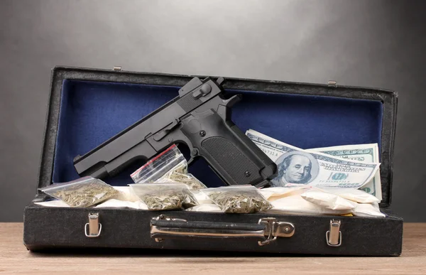 Kokaina, marihuana dolarów i pistolet w przypadku na drewnianym stole na szarym tle — Zdjęcie stockowe