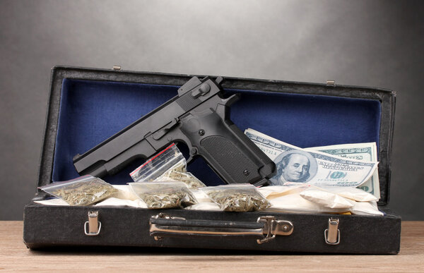 Кокаин, марихуана доллары и пистолет на случай, если на деревянном столе на сером фоне
