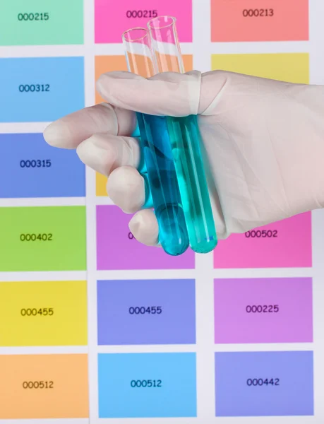 Two tubes with blue and dark blue liquid in hand on color samples background — Stock Photo, Image