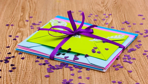 Куча цветных конвертов с лентой и конфетти на деревянном фоне — стоковое фото
