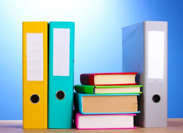 Яркие папки офиса и книги на деревянном столе на синем фоне — стоковое фото