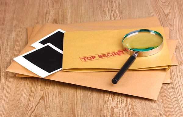 stock image Envelopes with top secret stamp with photo papers and magnifying glass on wooden background