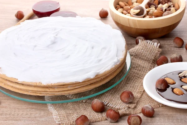 Cake on glass stand and nuts on wooden table — Stock Photo, Image