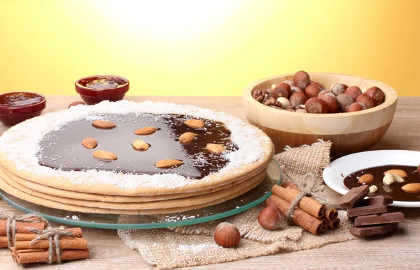 Kue di stand kaca dan kacang-kacangan di meja kayu dengan latar belakang kuning — Stok Foto