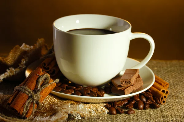 Taza de café y frijoles, palitos de canela y chocolate en el saqueo sobre fondo marrón —  Fotos de Stock