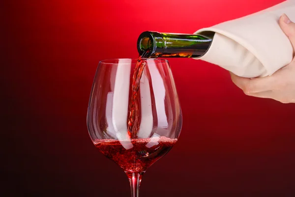 Nalil víno do sklenice na víno na červeném pozadí — Stock fotografie