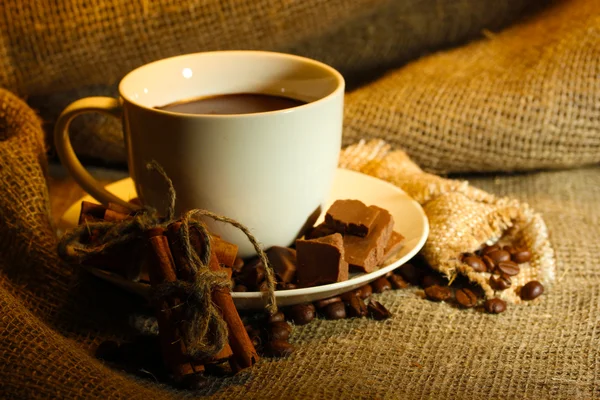 Чашка кофе и бобов, коричные палочки и шоколад на фоне мешка — стоковое фото