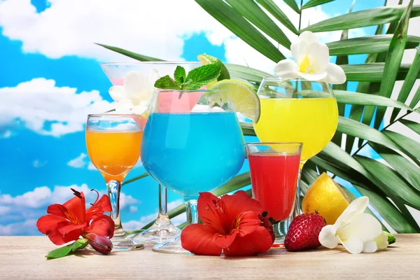 Cocktails exotiques et fleurs sur la table sur fond bleu ciel — Photo