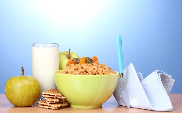 Вкусные кукурузные хлопья в зеленой миске, яблоки и стакан молока на деревянном столе на голубом фоне — стоковое фото