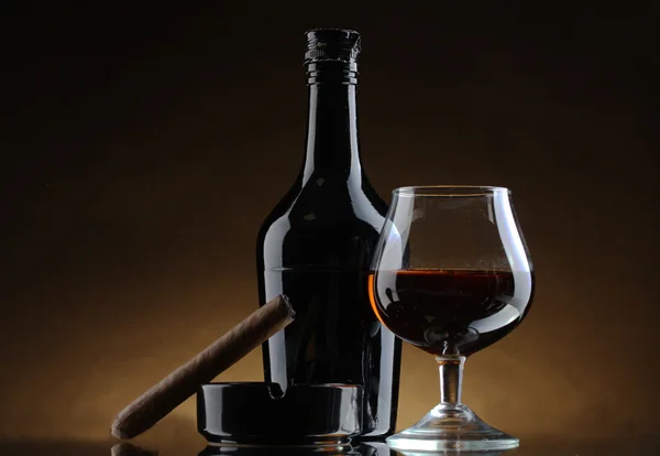 Botella y vaso de brandy y cigarro sobre fondo marrón —  Fotos de Stock