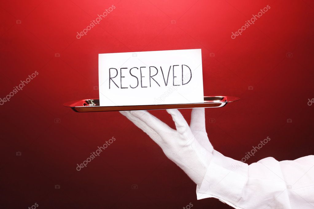 Hand in glove holding silver tray with card saying reserved on red background