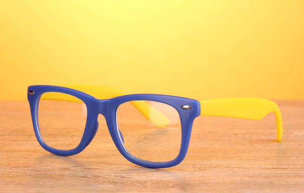 Красивые цветные очки на деревянном столе на желтом фоне — стоковое фото