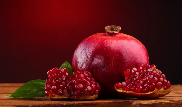 빨간색 배경에 나무 테이블에 잘 익은 석류 열매와 잎 — 스톡 사진