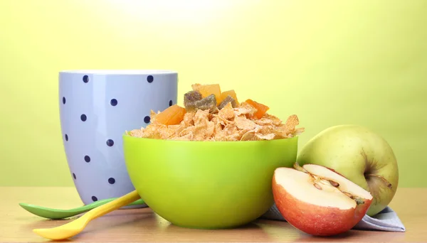 Välsmakande cornflakes i grön skål, äpplen och glas mjölk på träbord på grön bakgrund — Stockfoto