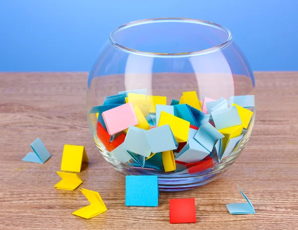 Кусочки бумаги для лотереи в вазе на деревянном столе на синем фоне — стоковое фото