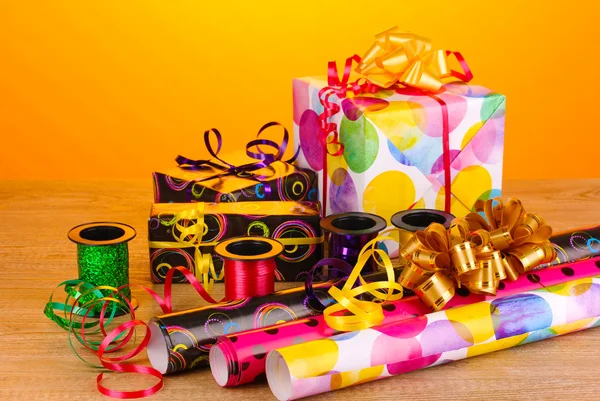Gigts, paper, ribbon and bows on wooden table on yellow background — Stock Photo, Image