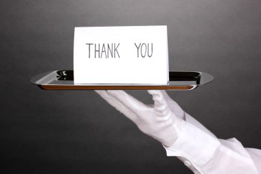 Hand in glove holding silver tray with card saying thank you on grey background clipart