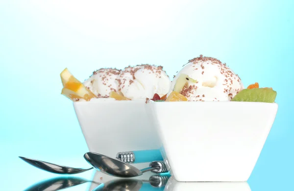 Вкусное ванильное мороженое с шоколадом и фруктами в мисках и ложках на синем фоне — стоковое фото
