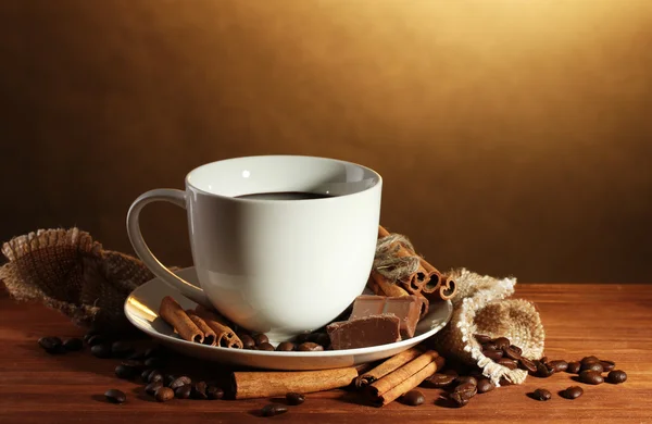 Kuppi kahvia ja papuja, kanelitankoja ja suklaata puupöydällä ruskealla pohjalla — kuvapankkivalokuva
