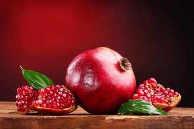 Ripe pomegranate fruit with leaves on wooden table on red background clipart