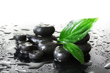 Spa stones with drops and green leaves on grey background clipart