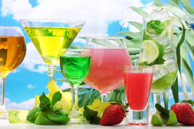 Glasses of cocktails on table on blue sky background clipart