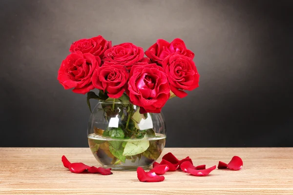 Beautiful red roses in vase on wooden table on gray background — Stock Photo, Image