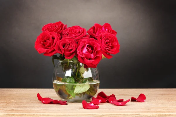 stock image Beautiful red roses in vase on wooden table on gray background