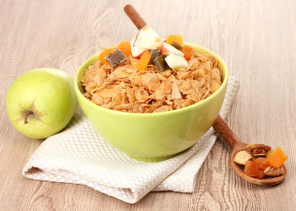 Tasty cornflakes in bowl with dried fruits and apple on wooden table — Stock Photo, Image