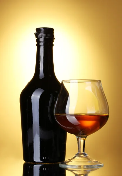 Glas Schnaps und Flasche auf gelbem Hintergrund — Stockfoto
