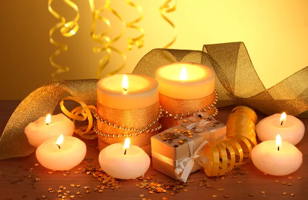 Piękne świece, prezenty i dekoracje na drewnianym stole na żółtym tle — Zdjęcie stockowe