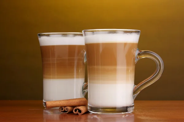 Geurige? offee latte in glazen bekers en kaneel op houten tafel op bruine achtergrond — Stockfoto