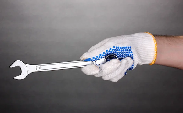 Schraubenschlüssel in der Hand mit Schutzhandschuh auf grauem Hintergrund — Stockfoto
