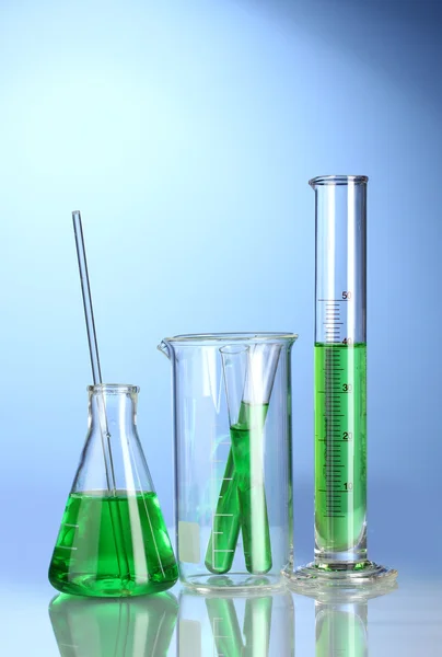 Vetreria da laboratorio con liquido verde con riflessione su fondo blu — Foto Stock