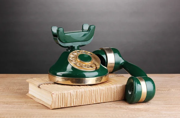 Ретро-телефон, стоящий на книге на деревянном столе на сером фоне — стоковое фото