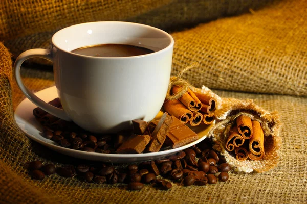 Taza de café y frijoles, palitos de canela y chocolate sobre fondo de saco — Foto de Stock