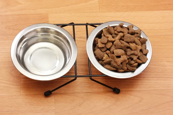 Dry dog food and water in metal bowls on the floor — Stock Photo, Image