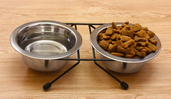 Сухий собака їжа і вода в металевих мисках на дерев'яному фоні — стокове фото