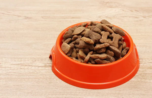 Comida de cão seco em tigela de laranja no fundo de madeira — Fotografia de Stock