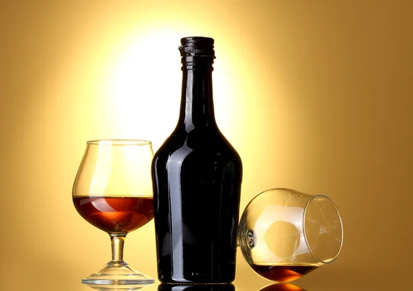Brýle brandy a láhev na žlutém podkladu — Stock fotografie