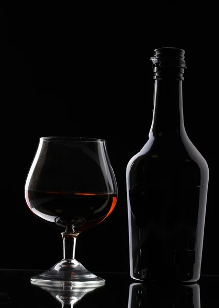 Copo de conhaque e garrafa sobre fundo preto — Fotografia de Stock
