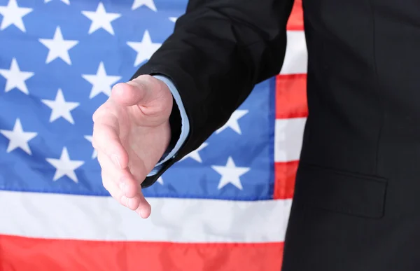 Empresário dando a mão por um aperto de mão no fundo da bandeira americana — Fotografia de Stock