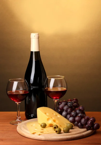 Bottle of great wine with wineglasses and cheese on wooden table on brown background