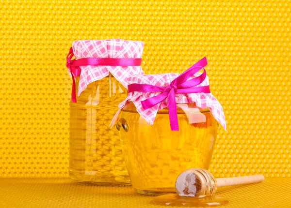 Jars of honey and wooden drizzler on yellow honeycomb background — Stock Photo, Image