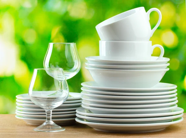 Clean dishes on wooden table on green background — Stock Photo, Image