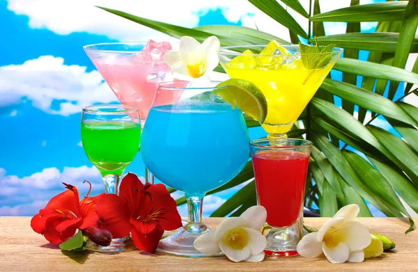 Egzotik kokteyller ve mavi gökyüzü arka plan üzerinde masaya çiçek — Stok fotoğraf